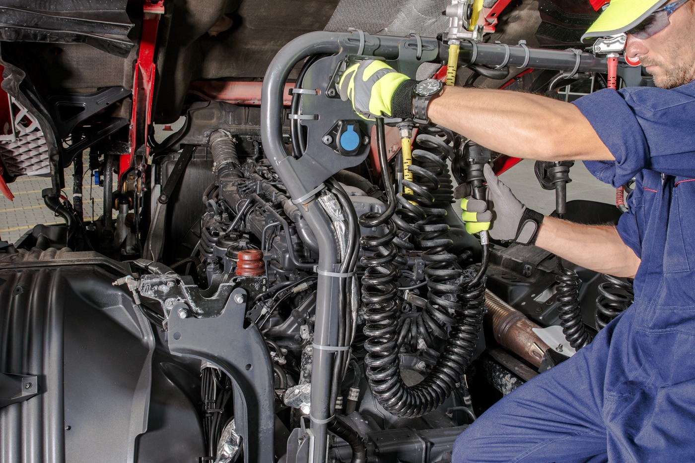A mechanic works on the engine bay of a large truck, connecting hoses and equipment, illustrating essential maintenance tasks for vehicles.